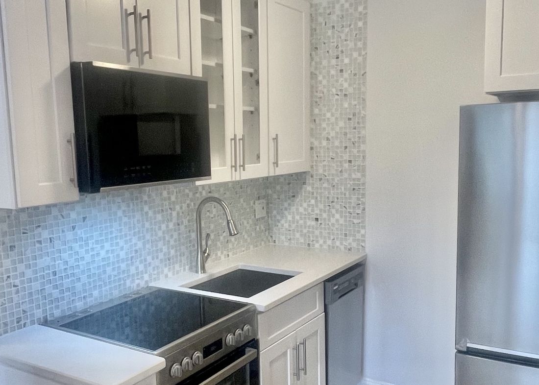 The same kitchen rebuilt with white shaker cabinets, quartz counters, mosaic tile and stainless appliances