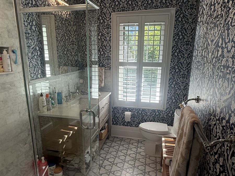Renovated bathroom with marble tile, patterned stone floor and custom wallpaper